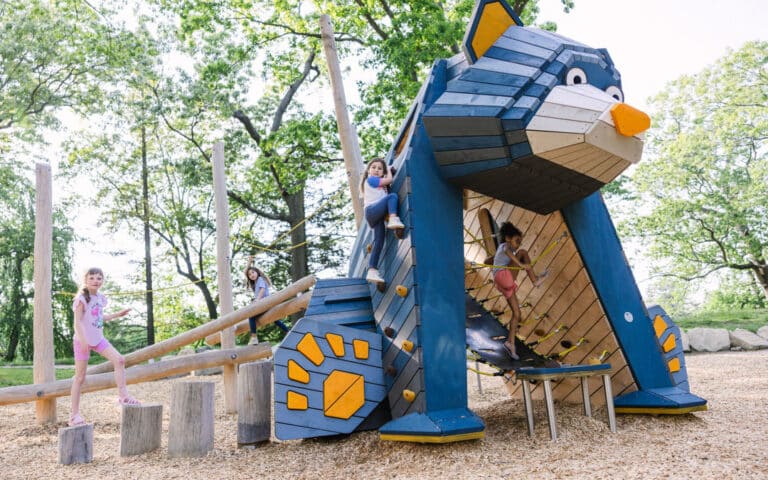 Children play on a custom wooden playground that looks like a blue bear
