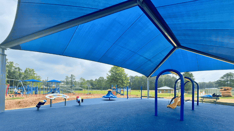 A blue shade structure covers a playground and swing set.