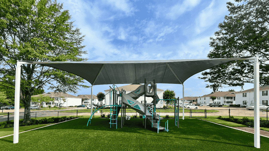 A large grey shade structure covers a playground on green turf.