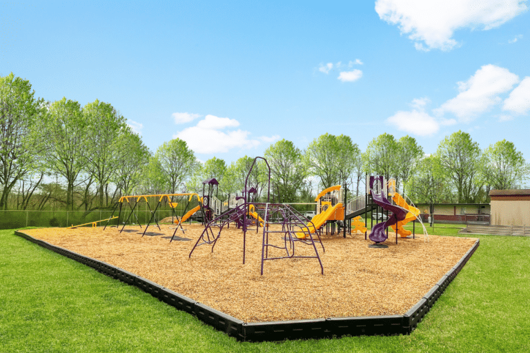 A purple and yellow playground. Mulch and grass surround the playground.