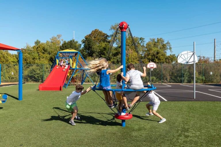 Five children play on a spinning playground climber. The grass is green and the climber is blue.