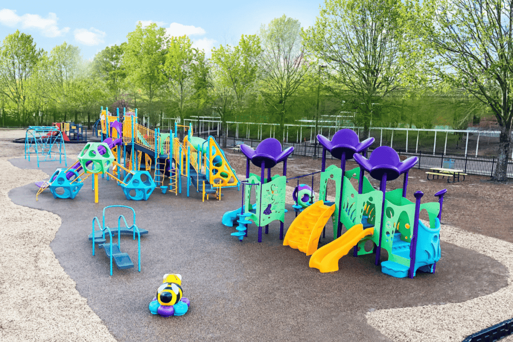 An overhead aerial photo of a school playground. The playground is purple, green, blue and yellow. Trees line the playground.