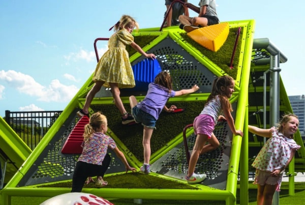Children climb up a commercial playground climber with custom baseball steps in this cover image of the Playworld 2026 Buyer's Guide.