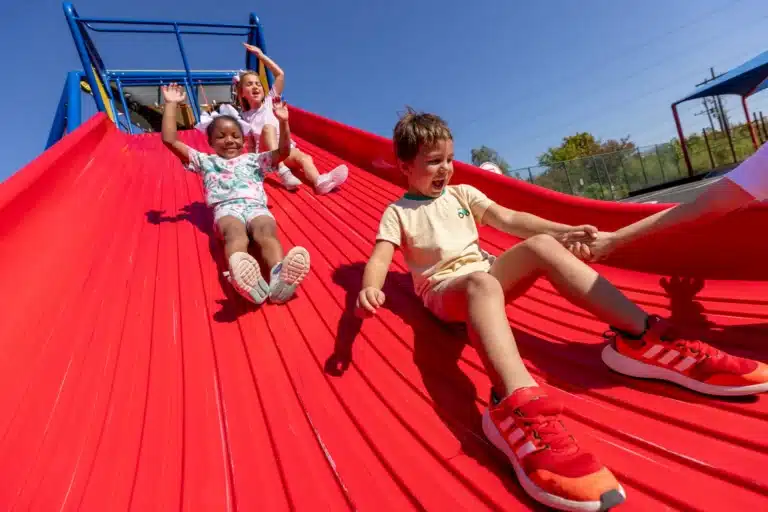 Three children slide down a large red slide together at the Dunham School in Louisiana.